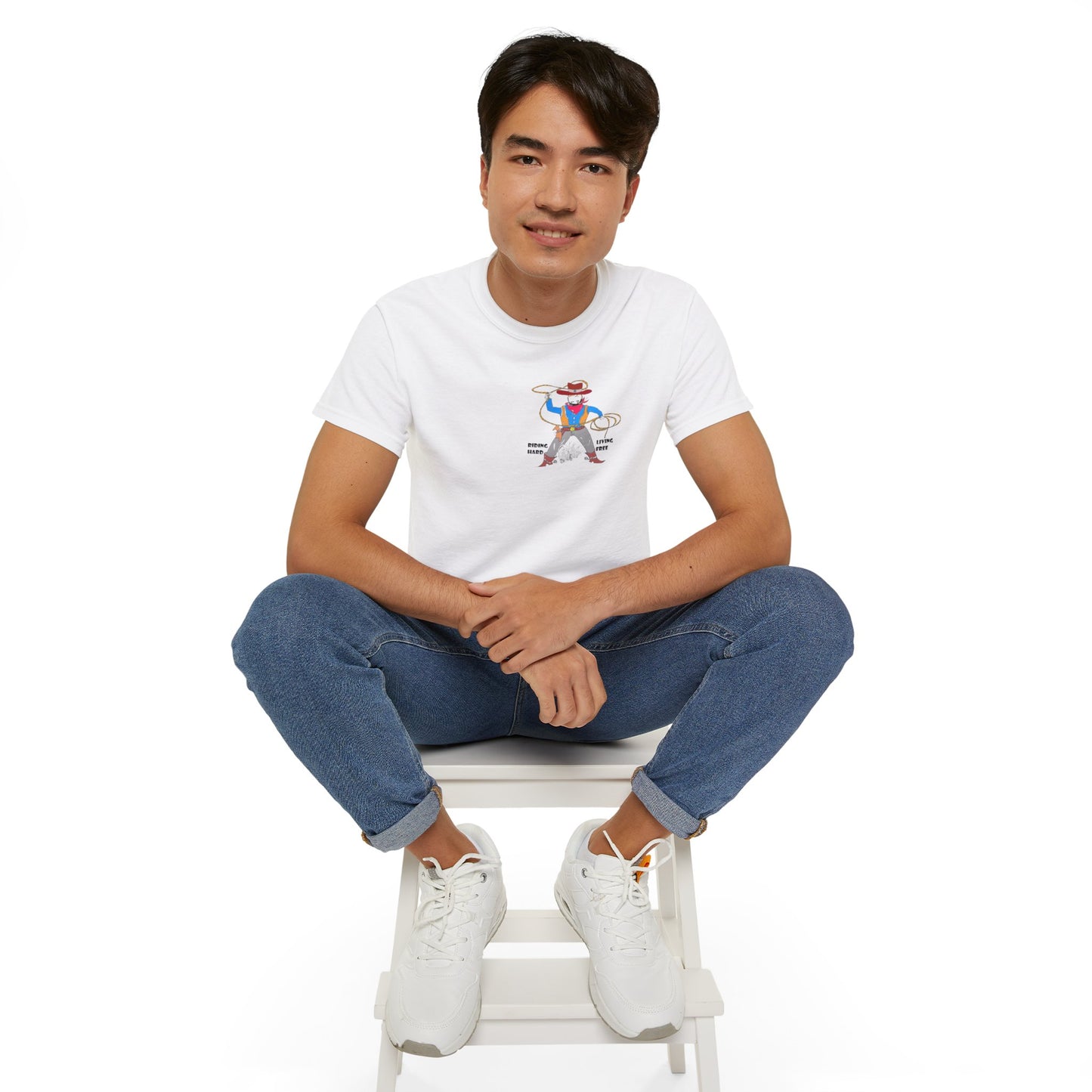 Front view of a man model wearing a white t-shirt with a cowboy graphic design, sitting on a white stool against a white background