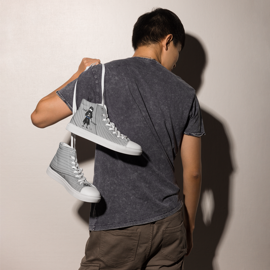 Person holding a pair of gray high-top sneakers with a ninja graphic design against a plain background