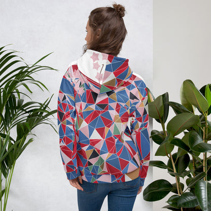 Person wearing a colorful geometric-patterned hoodie standing between two plants against a white wall.