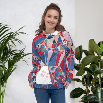 Woman wearing a colorful geometric-patterned hoodie with cherry blossoms graphic standing between two plants against a white wall.