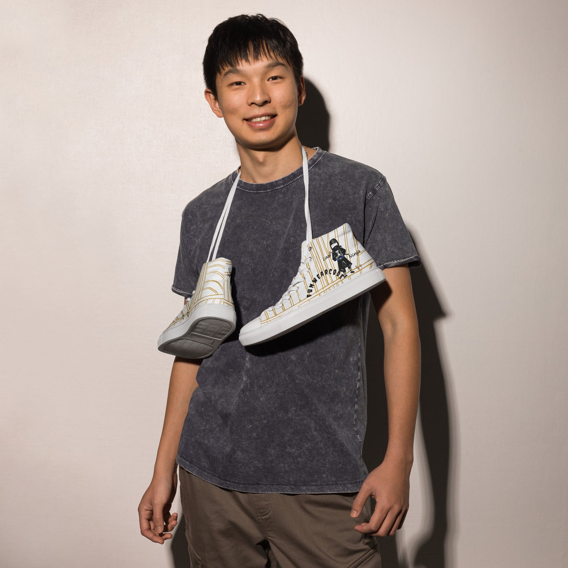 Person holding two white high-top sneakers with a ninja graphic and 'Fun Wear Code' text logo against a plain background
