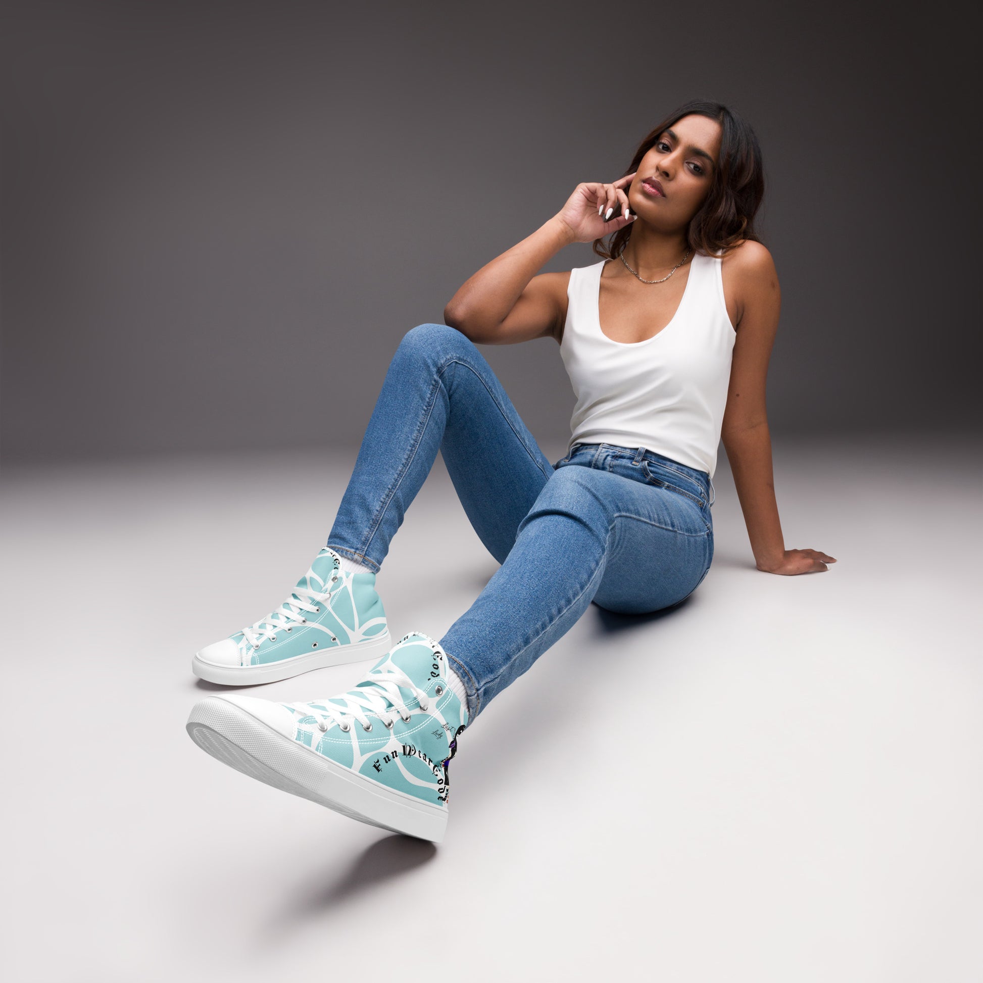Woman sitting on the floor wearing white high-top sneakers with a ninja graphic and 'Fun Wear Code' text logo, blue jeans, and a white tank top.